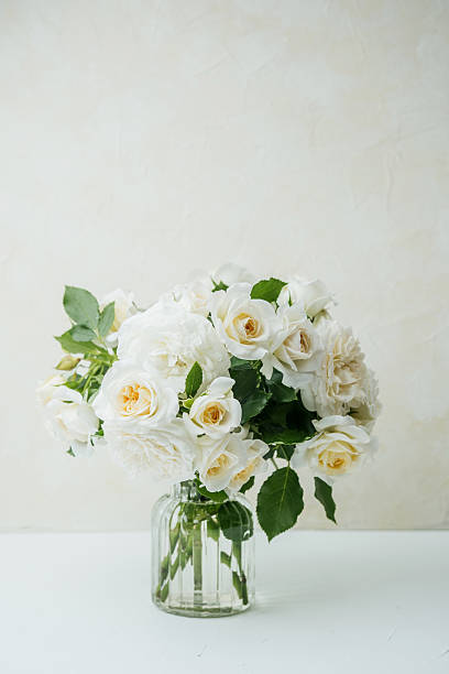 istock White roses bouquet in glass vase on white table with light background 2228817121