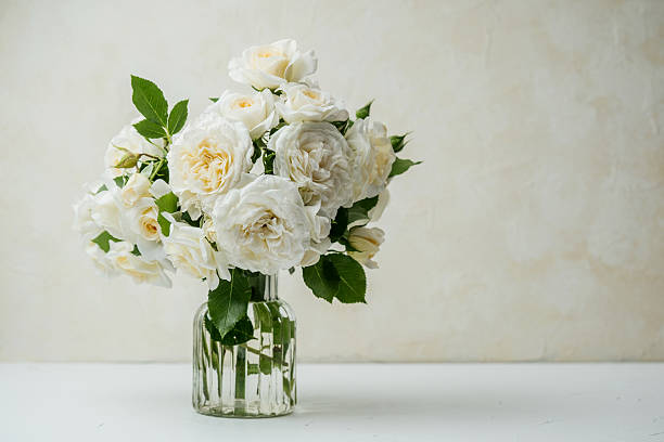 istock White roses bouquet in glass vase on white table with light background 2228817125
