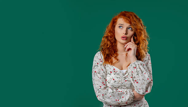 istock Thoughtful around red-haired curly woman On green. Puzzled Lady Looking Answer 2228834620