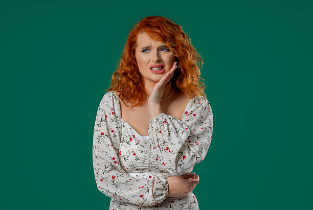 istock Bright red-haired woman with tooth pain, green studio. Toothache, dental problem 2228834626