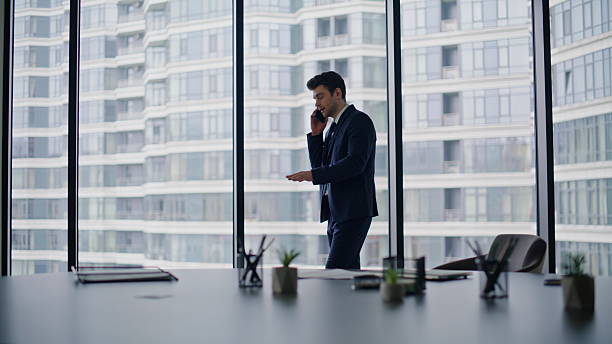 istock Elegant manager negotiating smartphone by office window. Businessman calling 2228836712