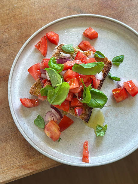 Stock photo shows a deconstructed bruschetta appetizer is artfully arranged with toasted bread, fresh tomatoes, garlic, and vibrant basil leaves, drizzled with pesto and olive oil. This elegant starter showcases the flavors of Italian cuisine in a modern presentation