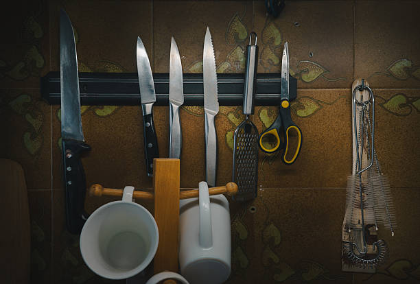 Kitchen knives and other accessories on a magnetic strip on the wall with decorative tiles.