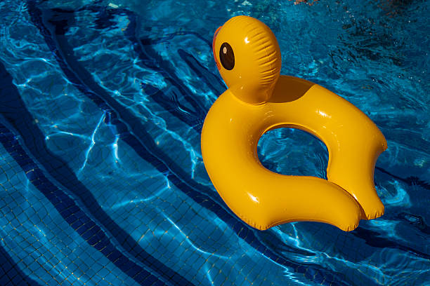 istock Bright yellow inflatable duck ring floating alone in a clear blue swimming pool, creating a playful summer atmosphere with sunlight reflecting off the water and tiled surface underneath 2228842834