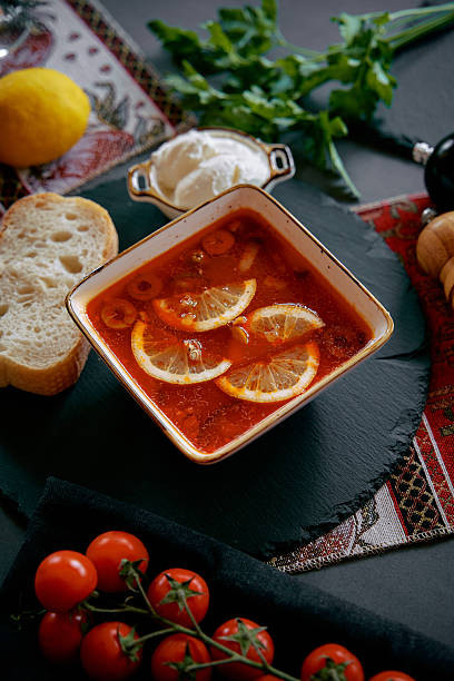 A Delicious Bowl of Comforting Tomato Soup Garnished with Fresh Lemons, Accompanied by Bread and Cherry Tomatoes on a Vibrant Table Setting