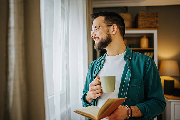 istock Young man enjoying a book and coffee by the window 2228847001