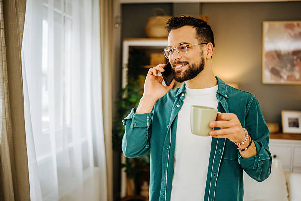 istock Young man talking on smartphone and drinking coffee at home 2228847023