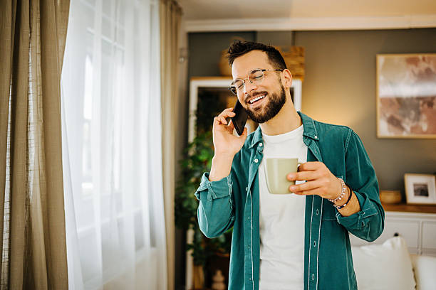 istock Young man talking on the phone and drinking coffee at home 2228847026