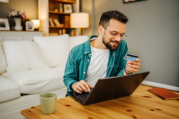istock Young man making online payment using laptop and credit card at home 2228847044