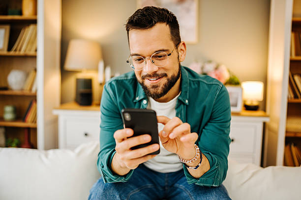 istock Young man is sitting on sofa at home and using smartphone 2228847112