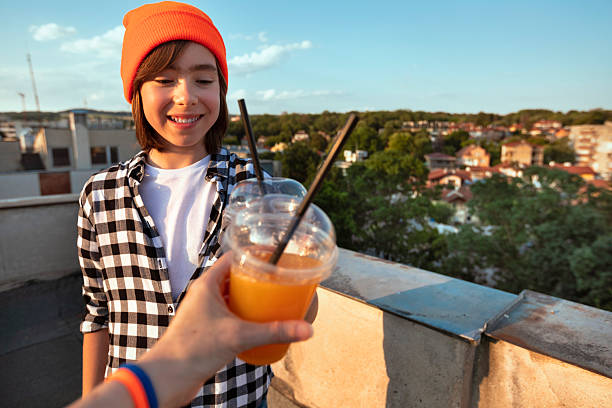 Cool-looking children enjoy fresh juice while hanging out on a rooftop, with an urban view stretching out behind them.
