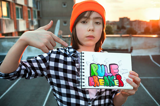Portrait of a serious boy poses on a rooftop, holding a “rule breaker” drawing with the city glowing at sunset.