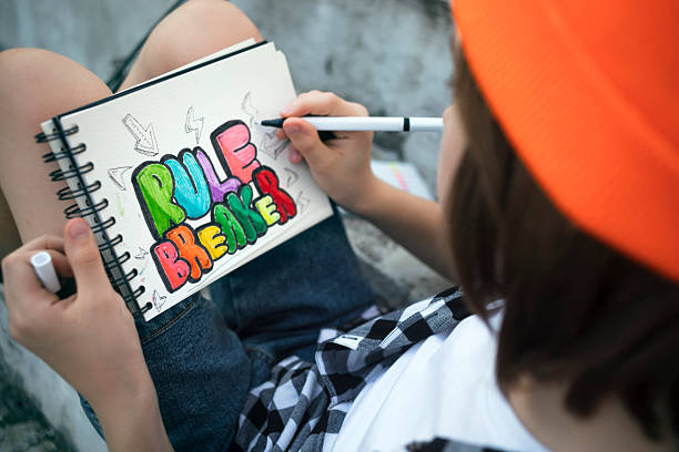 istock Child writing “rule breaker” in sketchbook on city steps 2228857501