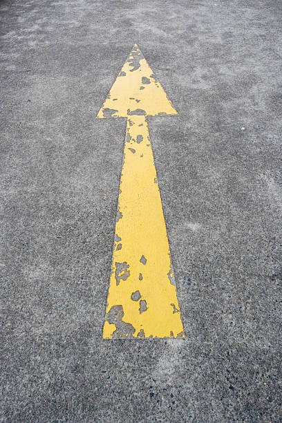 Faded yellow direction arrow painted on a gray concrete floor.