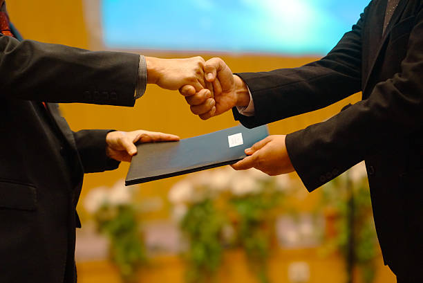 istock Meeting success. Two businessmen are shaking hands and exchanging contract documents. 2228861696