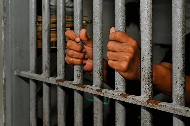 istock prisoner's hands behind bars with black background 2228870162