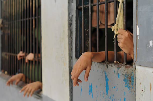 istock prisoner's hands behind bars with black background 2228870206