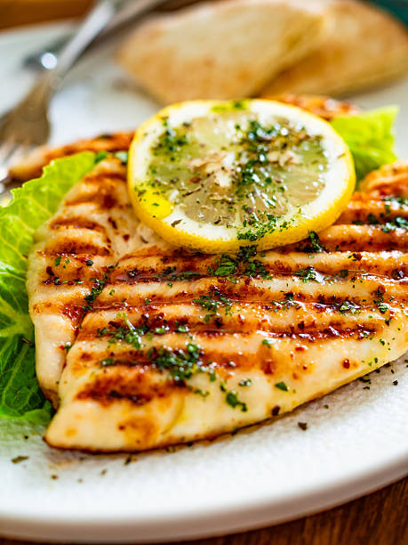 Barbecued chicken breast, pita bread and tzatziki served on black stony board on wooden table
