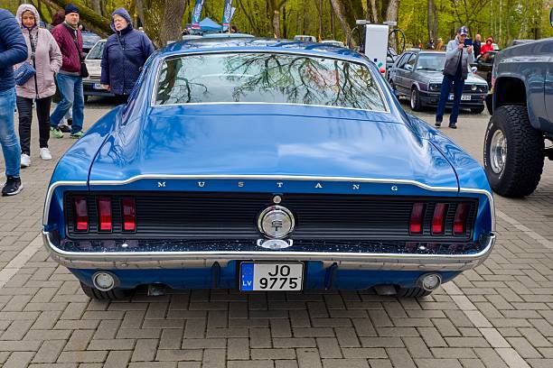 Liepaja, Latvia, May 17, 2025 - A rear view of a beautifully restored classic blue Ford Mustang, showcasing its iconic tail lights, chrome details, and retro styling. The car is parked at an outdoor car event, surrounded by people and other vehicles, emphasizing its vintage charm and automotive heritage.