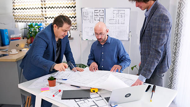 istock A man with a triangle ruler points to the drawings and asks the architect for the construction time of the facility. There are three businessmen at the table 2228878676