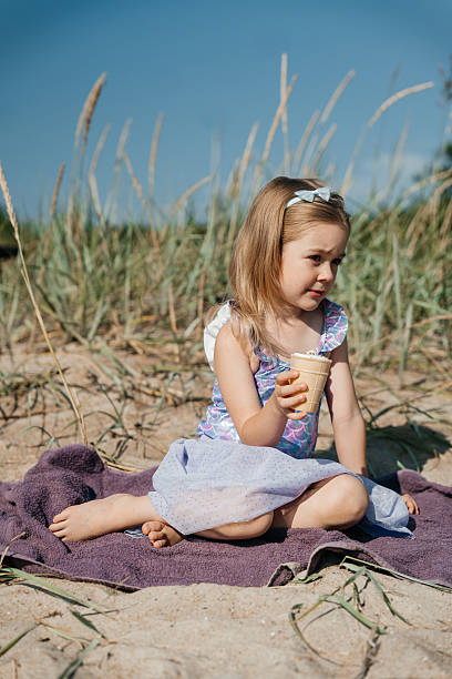 istock Child enjoying ice cream on sandy beach surrounded by tall grass during sunny day 2228884336