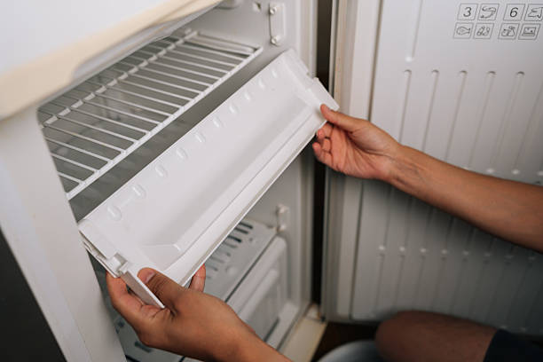 istock Man preparing to removing ice tray from refrigerator during defrosting, suggesting thorough cleaning process for household appliance maintenance. 2228888379