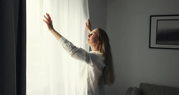 Woman opening window curtains at home in morning stock photo