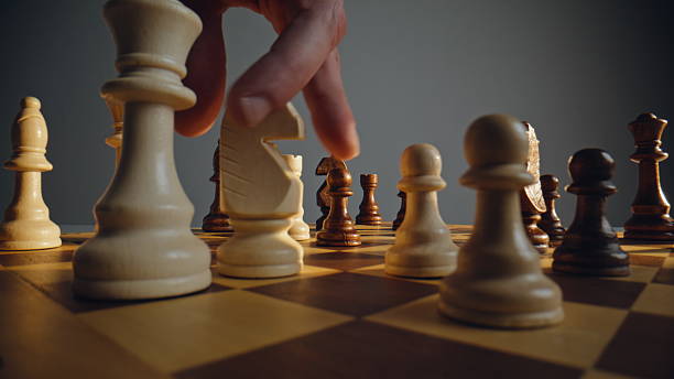 istock Hand directing ivory chess across grid with rival troops closeup. Strategic game 2228890145