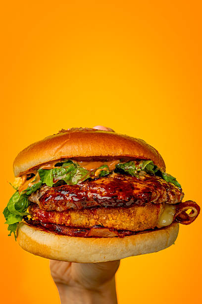 istock Hand holding a bright juicy burger on an orange background 2228891024