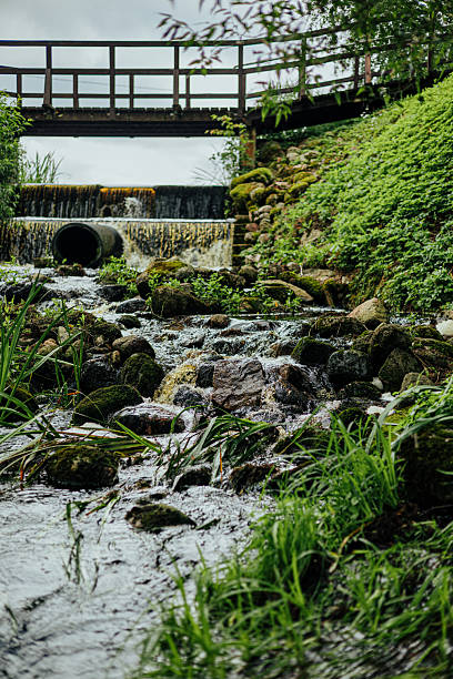 istock Small Forest Stream with Bridge and Mossy Rocks 2228891420