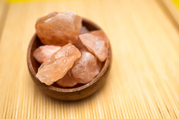 Close up studio shot of Himalayan salt stones, large pieces, placed on a yellow background in a jar and a wooden bowl. No people.