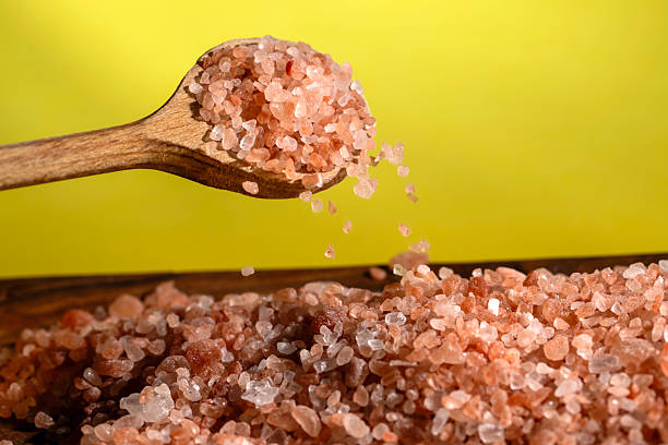Himalayan salt - pouring from a wooden spoon - yellow background