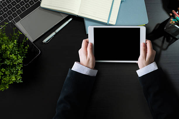 Male hands working on modern tablet computer. Office desktop on black background. Top view with copy space, flat lay.