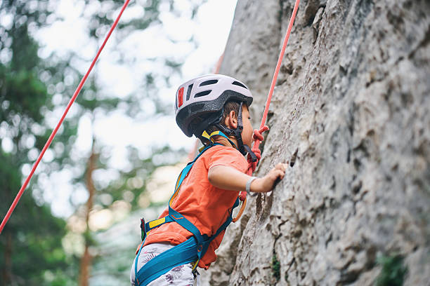 Side view of young boy climbing rock wall with helmet and harness