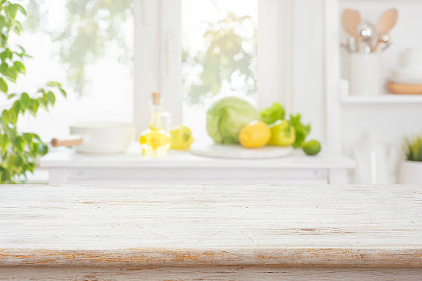 Bleached empty wooden table with bright interior of kitchen counter and window as blurred background
