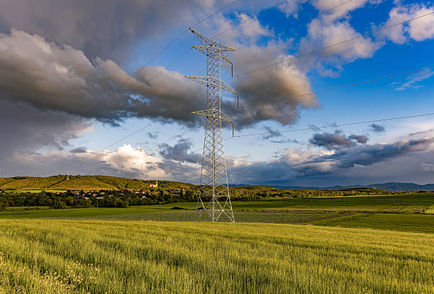 A dramatic shot of a field with dark cloudy sky and a transmission metal tower in the center