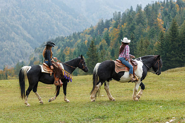 A girl in sunglasses with a white horse wearing a red bridle against a background of mountains and a blue sky