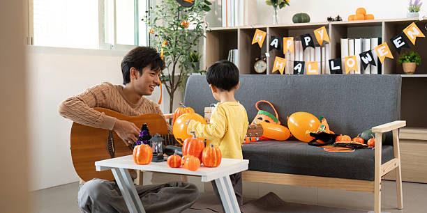 Musical Halloween. Father playing guitar while son enjoys pumpkin decorating.