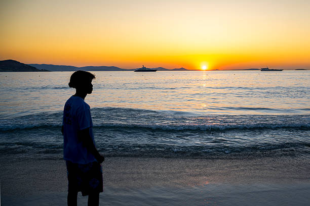 Silhouette of a man sitting on a wooden structure watching the sunset by the sea