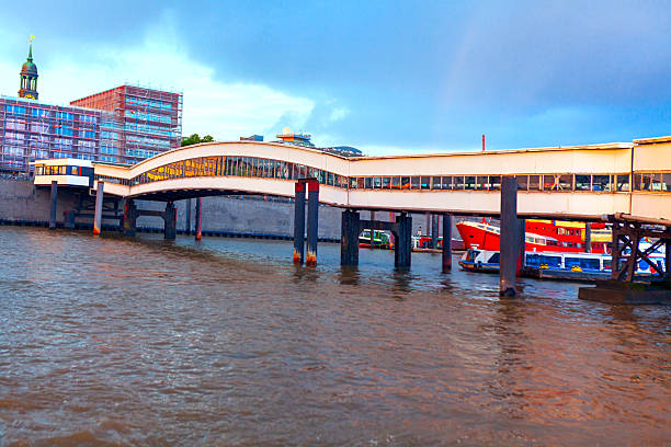 Uberseebrucke bridge over Elbe river in Hamburg. Pedestrian bridge spans a waterway, offering a view of the city skyline and harbor traffic in Germany