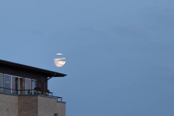 Half moon on cloudy blue sky with roof top view.\nCopenhagen - Denmark.