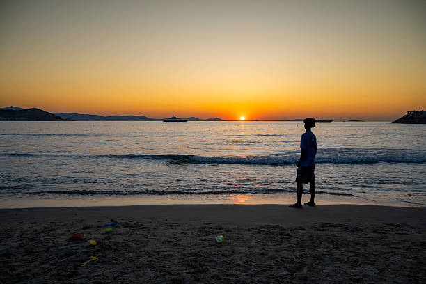 Silhouette of a person enjoying a tranquil sunset in Naxos, overlooking luxury yachts on the Aegean Sea. A serene scene symbolizing wealth, privacy, and the allure of Mediterranean living.