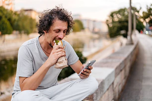 istock Mid-Adult Man Using Phone While Eating A Sandwich On The Quayside 2228912583