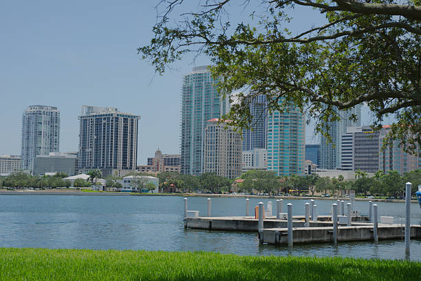 Urban skyline featuring tall buildings by a peaceful harbor under blue skies and fluffy clouds. A harmonious blend of nature with city life showcasing architecture and serenity.