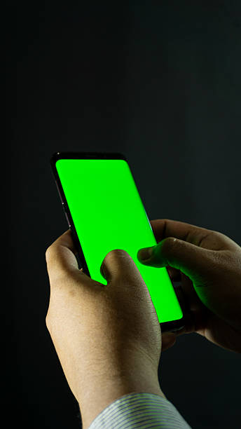 istock Two hands typing on smartphone with green screen, angled side view on black background, perfect for UI mockup or touchscreen interaction concept 2228921914