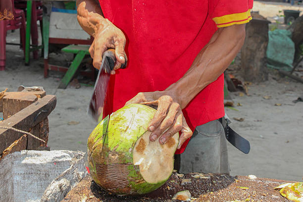 istock Craftsman skillfully opens a fresh green coconut using a sharp knife at an outdoor marketplace selling refreshing tropical beverages and providing an authentic island experience for tourists 2228925382