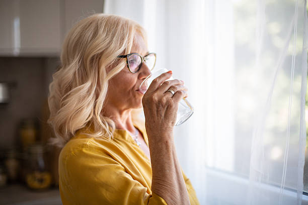 istock Senior woman drinking water by the window in a kitchen 2228930504