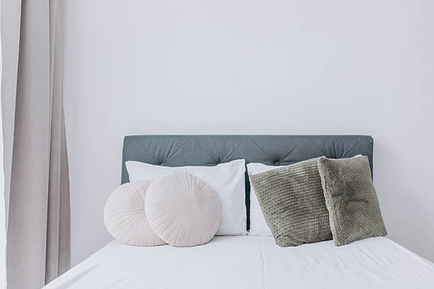 istock Symmetrical arrangement of decorative pillows on soft white bed with fabric headboard and curtains. 2228933095