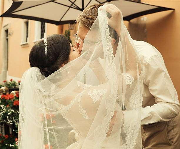 A happy bride and groom, holding hands, stroll through the city on their wedding day. The newlyweds, in love, take photos together.