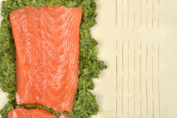 A high-angle shot of a fresh salmon fillet with a spinach and pesto filling on puff pastry, ready for baking